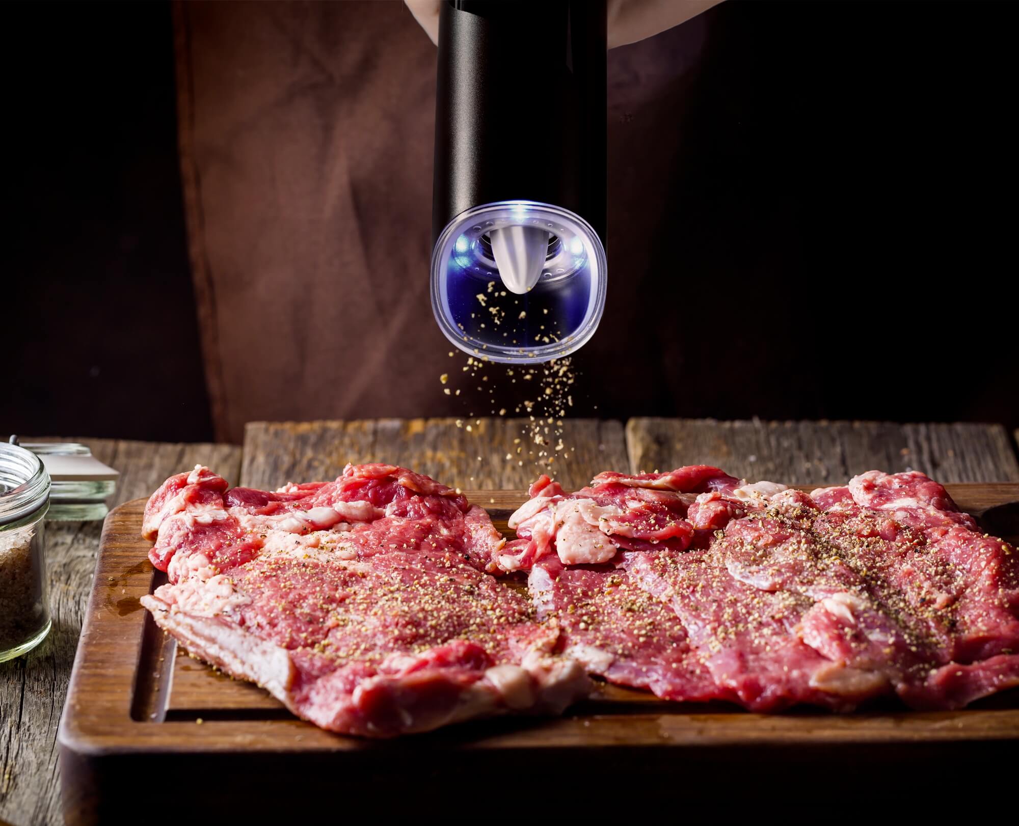 Man using Benchusch Modern Electric Gravity Pepper Grinder seasoning pepper to the raw meat on the dark background